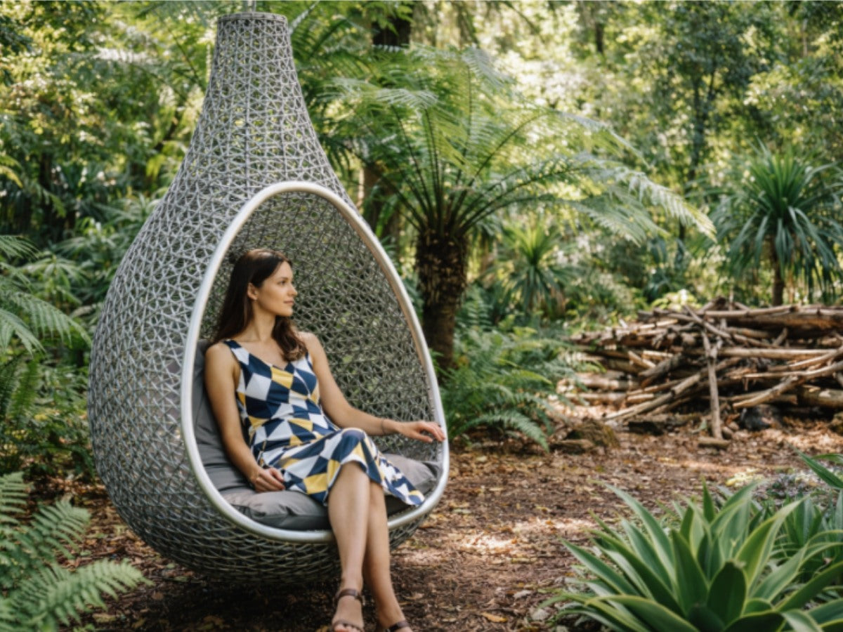 Woman relaxing in a modern hanging chair amidst ferns and native Australian plants at Royal Botanic Gardens Cranbourne